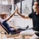 A boy sitting in a dental chair gives a high-five to a masked dentist wearing gloves in a bright dental clinic.